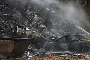 In this Nov. 10, 2015, file photo, a charred car and aircraft debris smolder where a small business jet crashed into an apartment building in Akron, Ohio. The National Transportation Safety Board is scheduled to meet in Washington on Tuesday, Oct. 18, 2016, to decide the probable cause of a corporate jet crash that killed the two pilots and seven passengers, and occurred within two miles of Akron Fulton International Airport while descending for landing. No one on the ground was injured. (Ed Suba Jr./Akron Beacon Journal via AP, File)