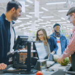 At the Supermarket: Checkout Counter Professional Cashier Scans Groceries and Food Items. Clean Modern Shopping Mall.