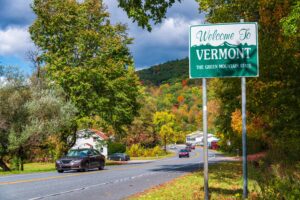 Welcome to Vermont state sign at road side with foliage in USA