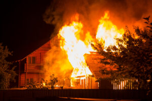 Burning wooden house at night. Bright orange flames and dense sm