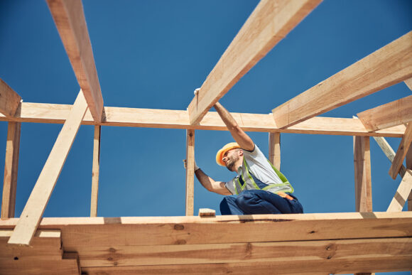 Kind builder working high on the roof of future house and wearing special uniform