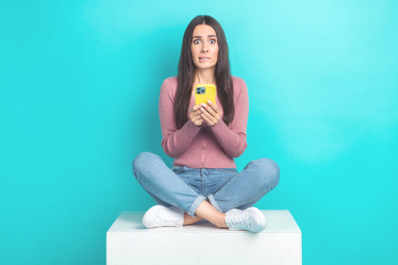 Full length photo of confused lady nervous bite lips hold her apple iphone terrified try dont remember password isolated on cyan color background.