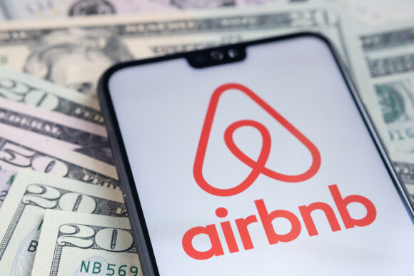 Stafford / United Kingdom - November 15 2020: Airbnb app logo seen on the screen of smartphone, placed on dollar bills.