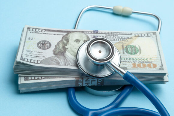 Stack of cash dollars and stethoscope on blue background. The concept of medical strechevka or expensive medicine, doctors salary