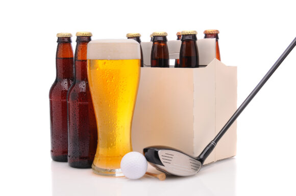 Six pack of beer and frothy glass with a Golf Club and ball in front. Horizontal format isolated on white with reflection.