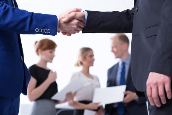 Close up of a business handshake, businesspeople in the background