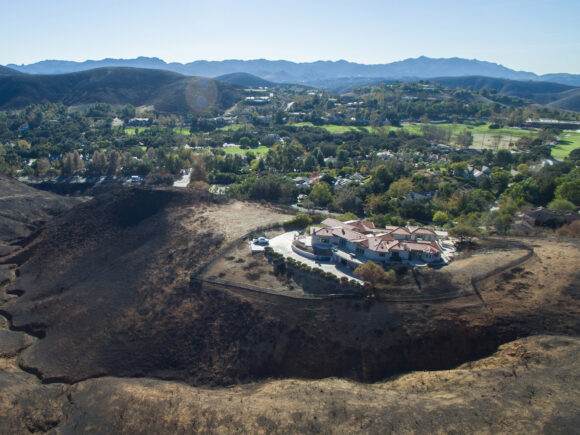 A lone house sits atop a charred hillside where a wildfire destr