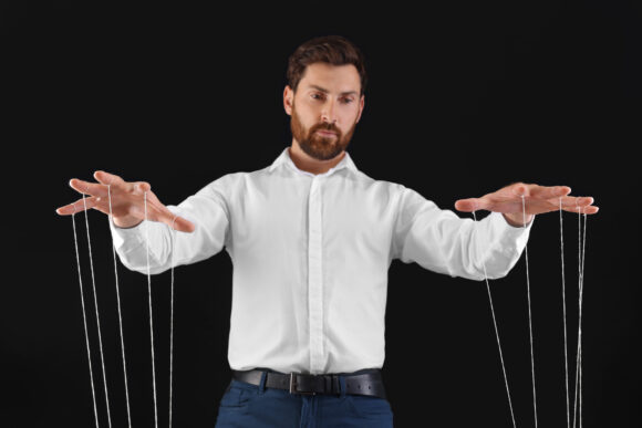 Man in formal outfit pulling strings of puppet on black background, low angle view