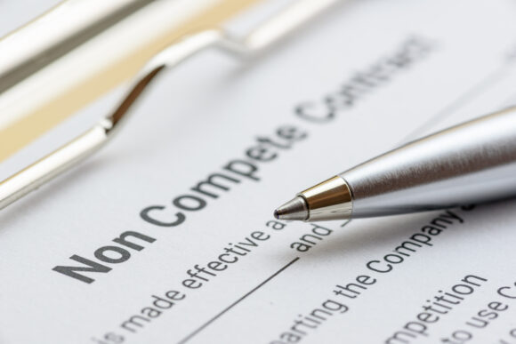 Blue pen, a gun or a pistol on a non compete contract. Noncompete contract is an agreement between employee and employer, not to enter into competition in subsequence business effort. Legal concept.