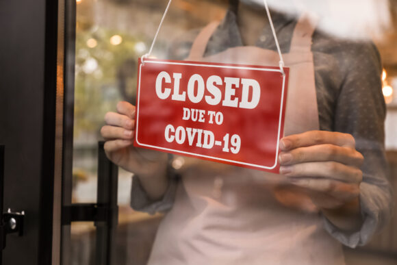 Woman putting red sign with words "Closed Due To Covid-19" onto