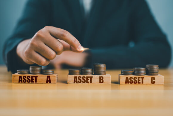 Diversify financial risk with funds. Investment asset allocation, diversification and risk management. Hand chooses on stacking coins with words ASSET A, B, C on wooden blocks. Real estate investment.