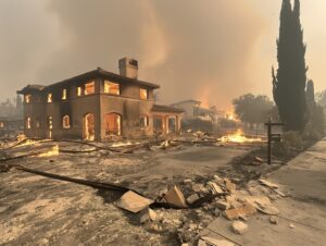 A house is on fire and the street is filled with debris. The house is surrounded by a tree and a sign