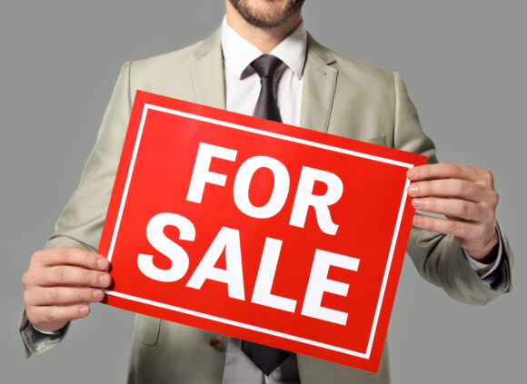 Real estate agent holding "For sale" sign on grey background